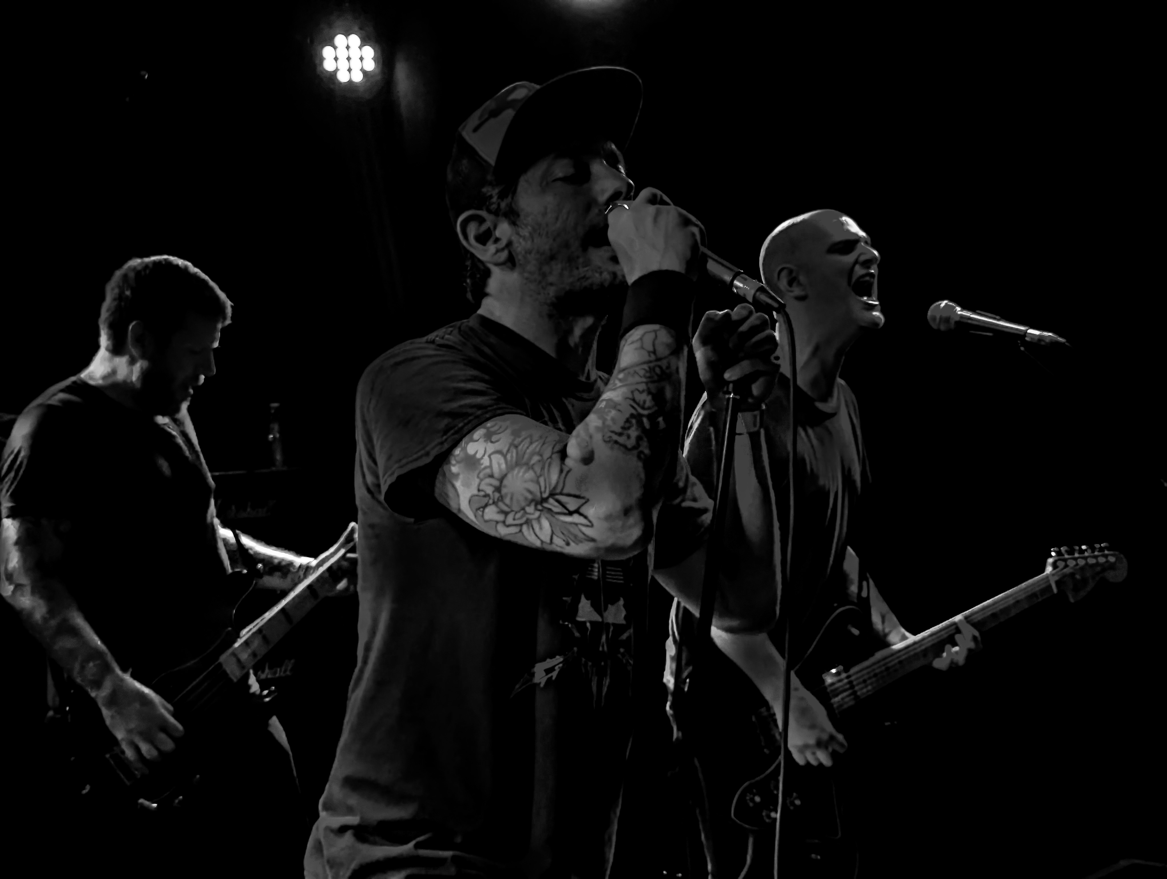 As Friends Rust performing, with a vocalist at the microphone and two musicians beside him